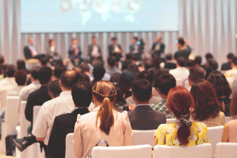 Rear view of audience in conference room listening to panel